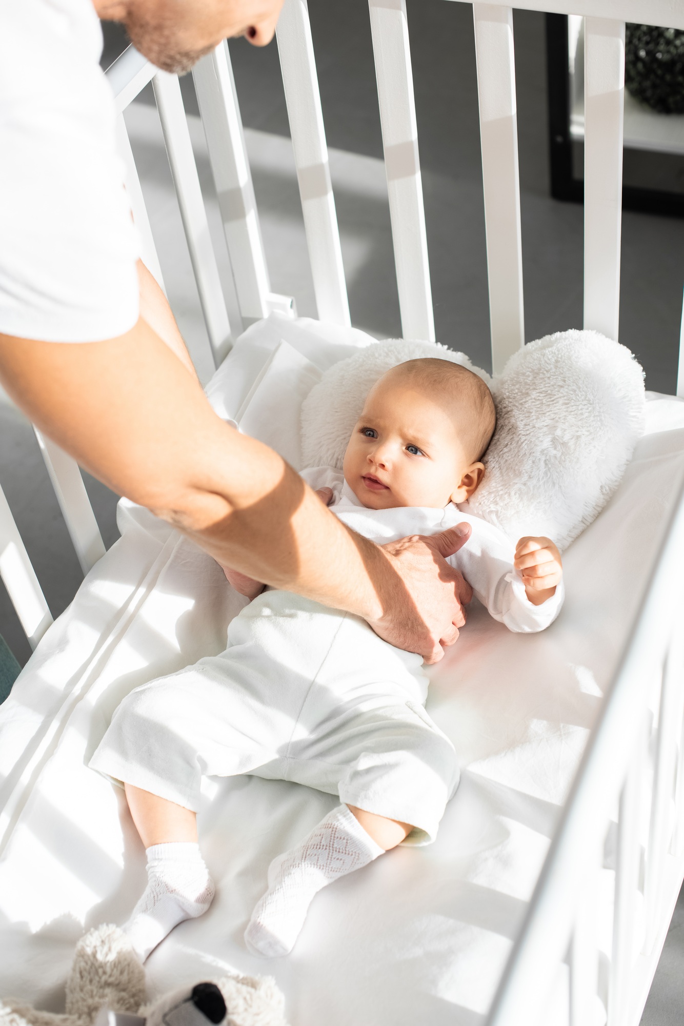 cropped view of father putting infant daughter into baby crib
