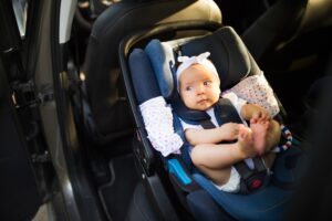 Little baby fastened with security belt in safety car seat.
