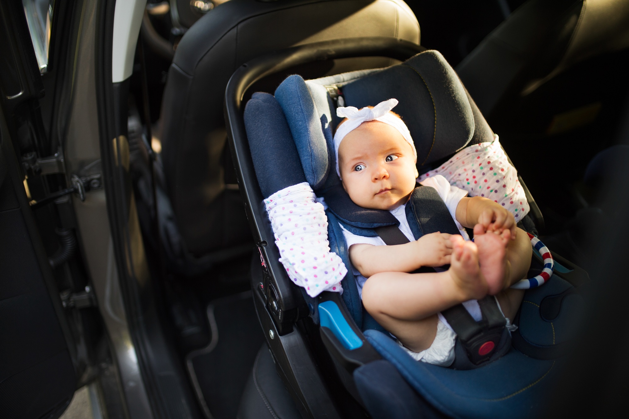 Home Little baby fastened with security belt in safety car seat.